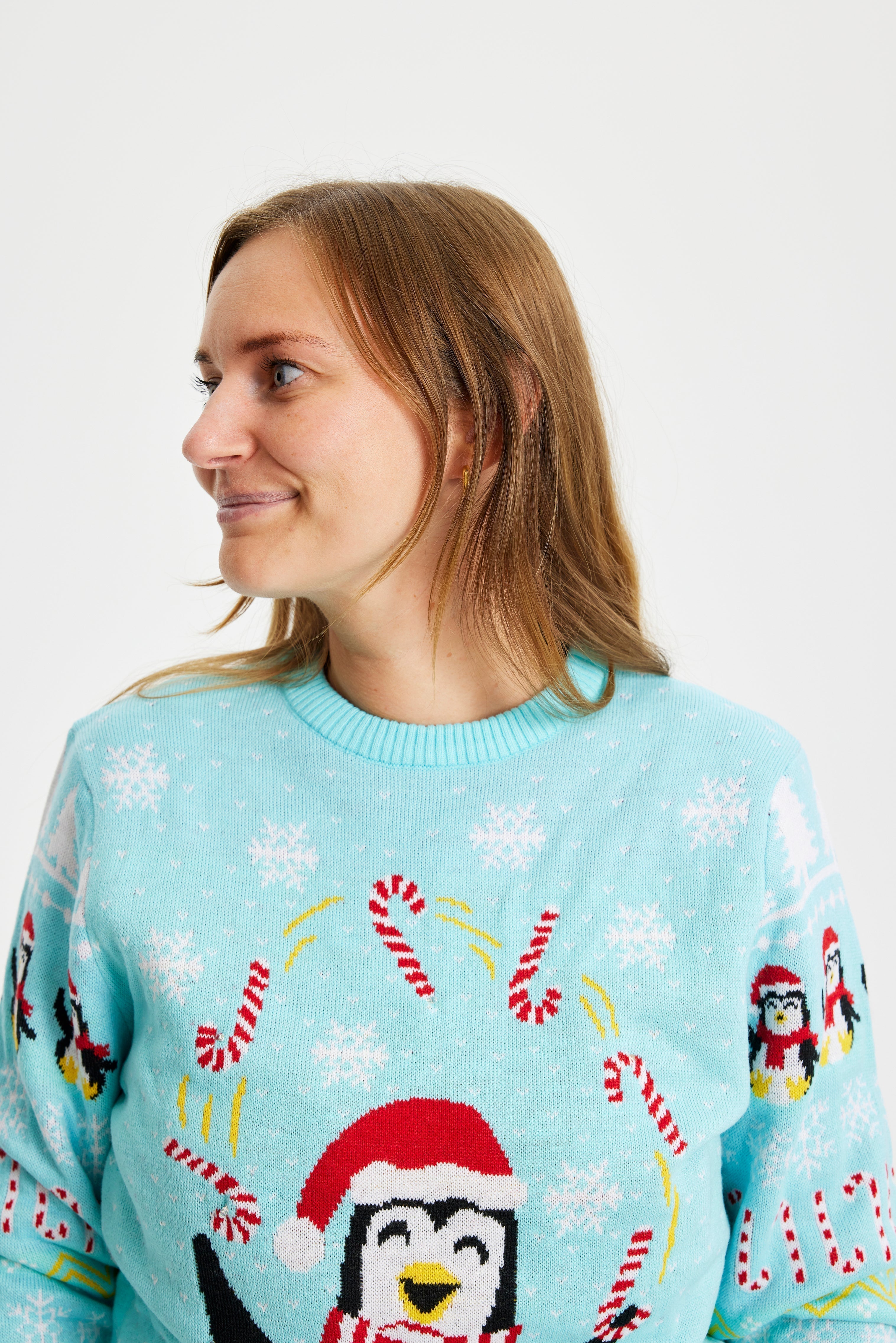 Une femme regardant de côté portant un pull de Noël bleu clair avec des pingouins et des lumières.